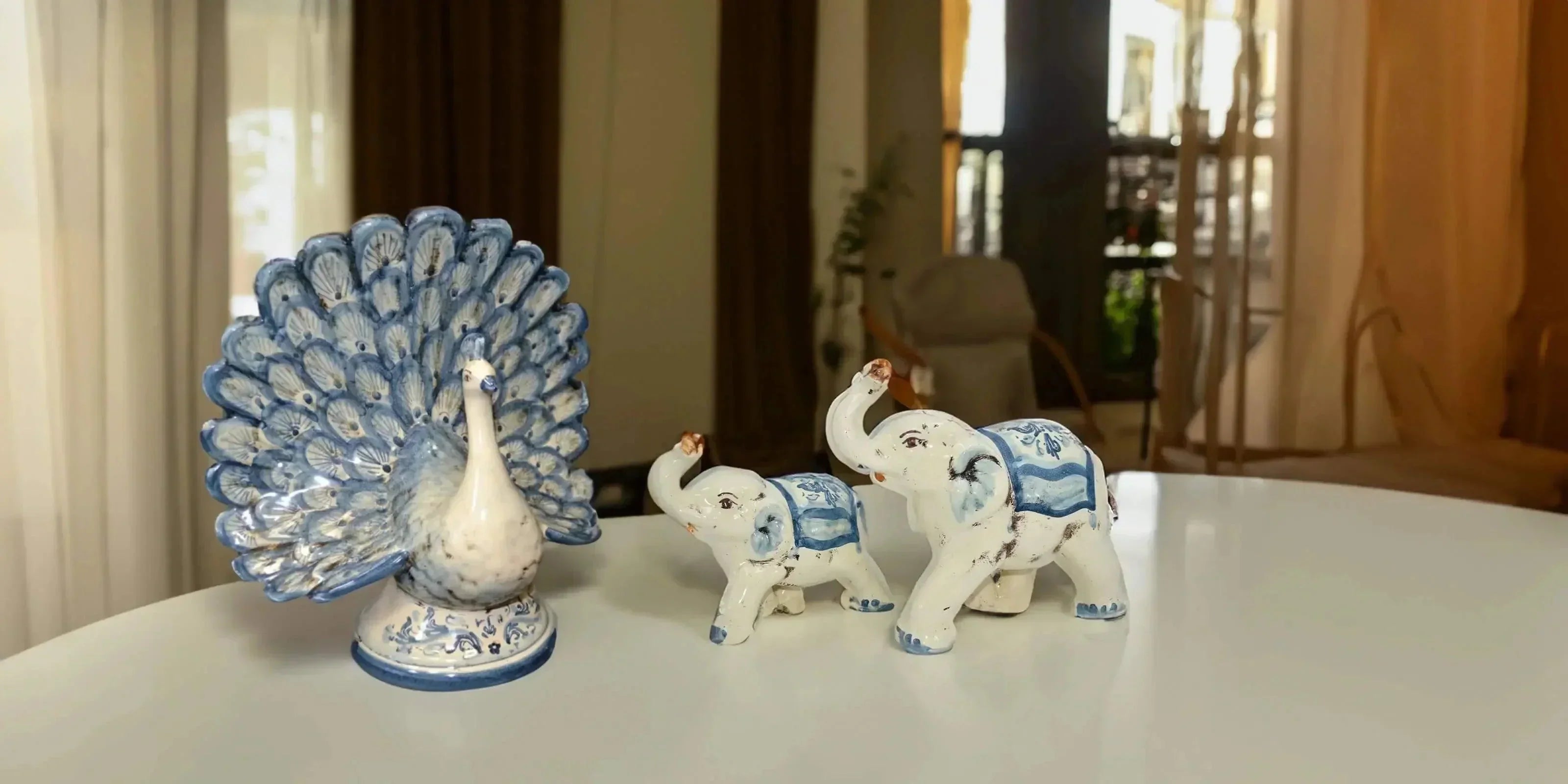 Animali in ceramica Caltagirone fatti a mano: pavone e elefanti su tavolo moderno.