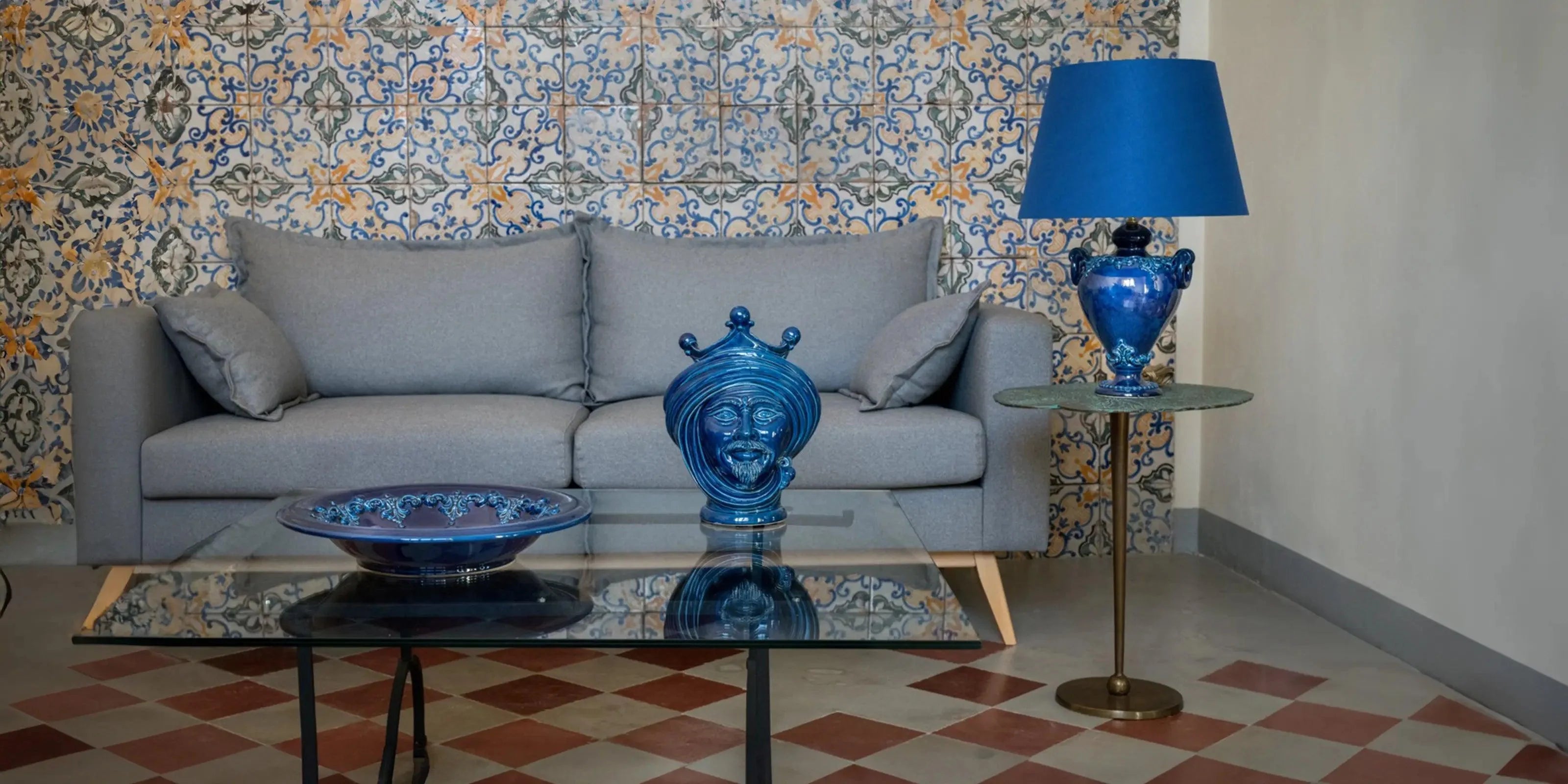Salotto con ceramiche Caltagirone fatti a mano blu, divano grigio e piastrelle decorate.