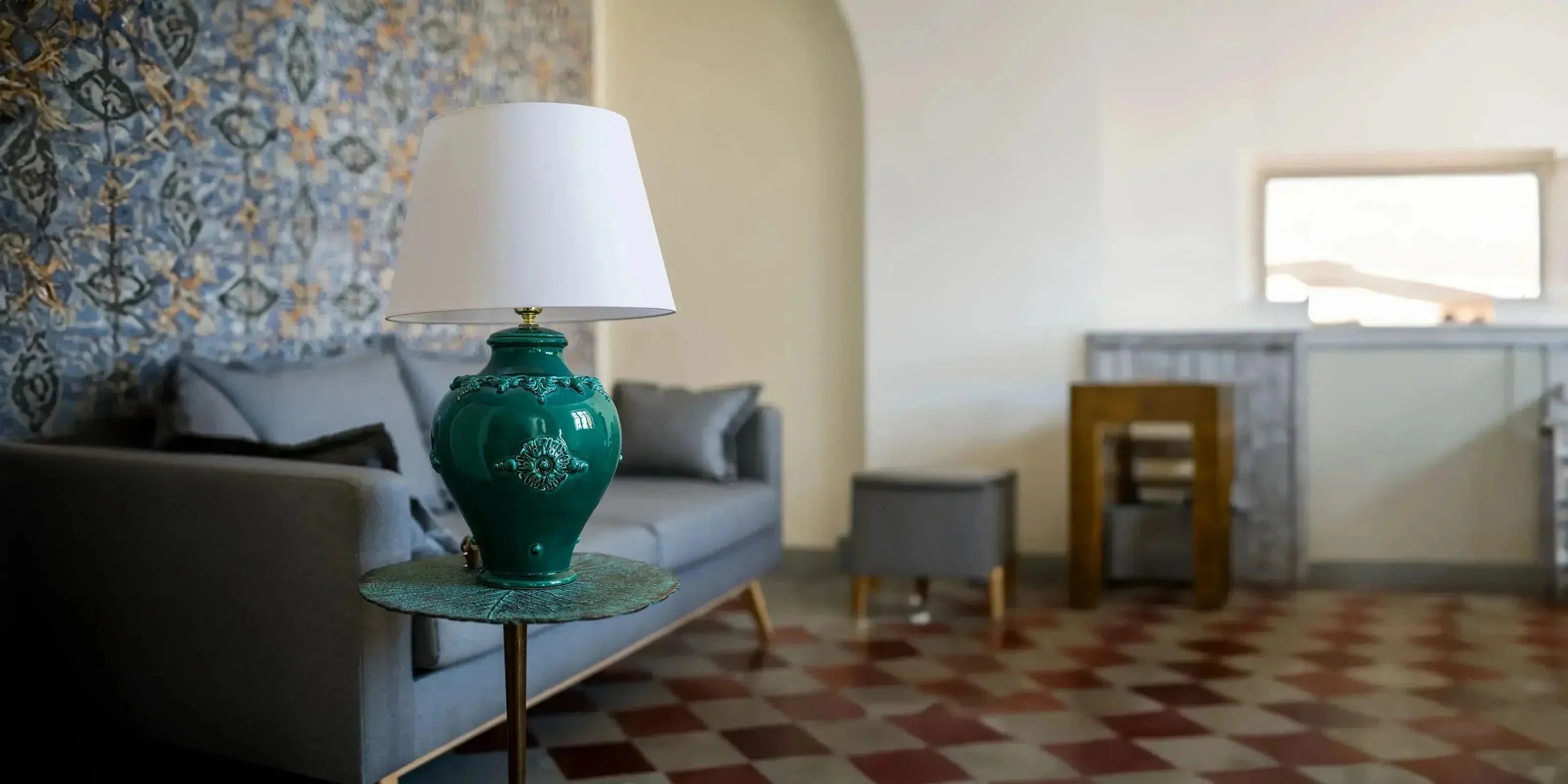 Lampada verde in ceramica di Caltagirone fatta a mano su tavolino in sala con divano grigio e parete decorata
