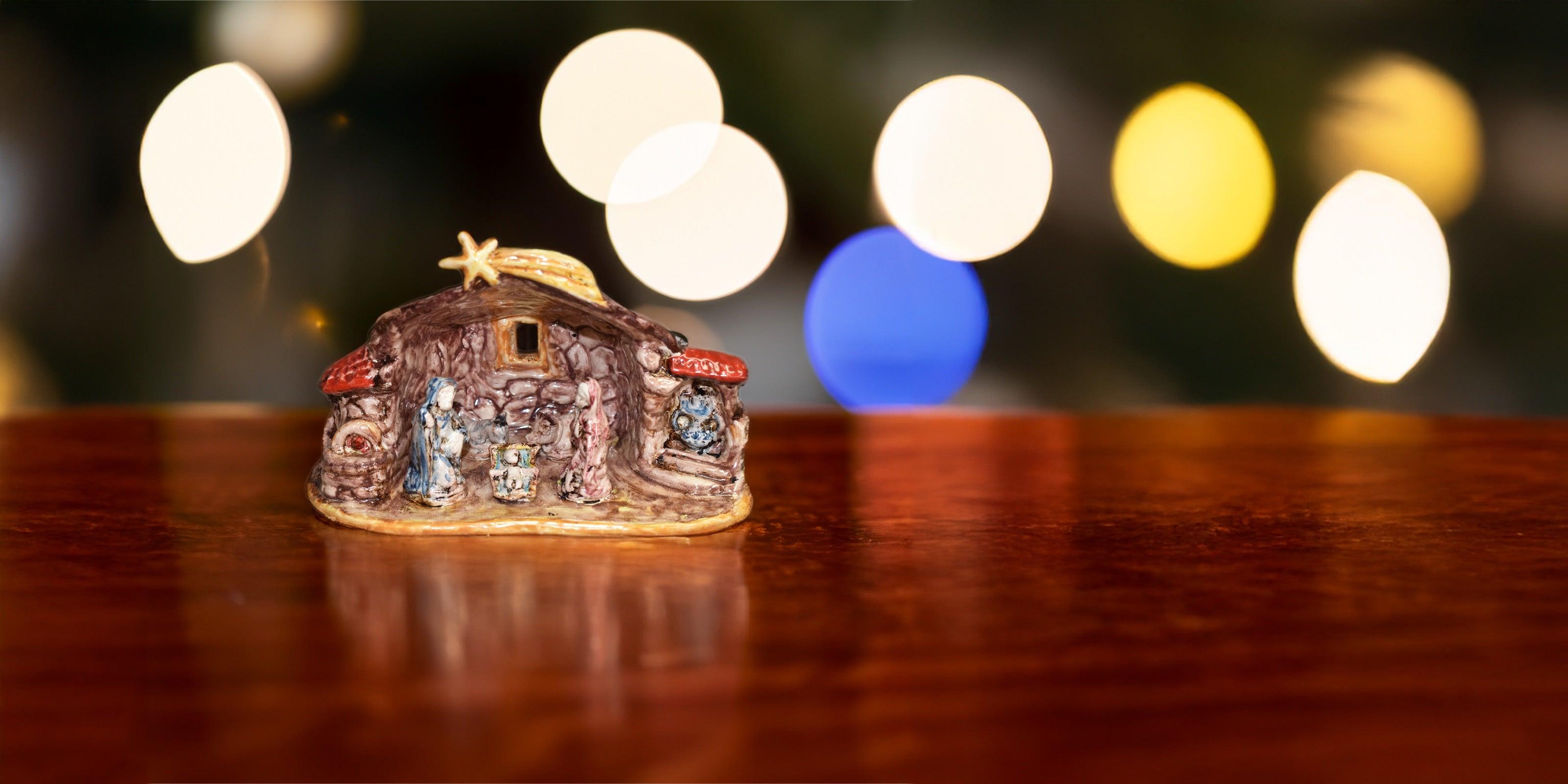 Presepe in ceramica di Caltagirone fatto a mano su tavolo di legno con luci sfocate sullo sfondo