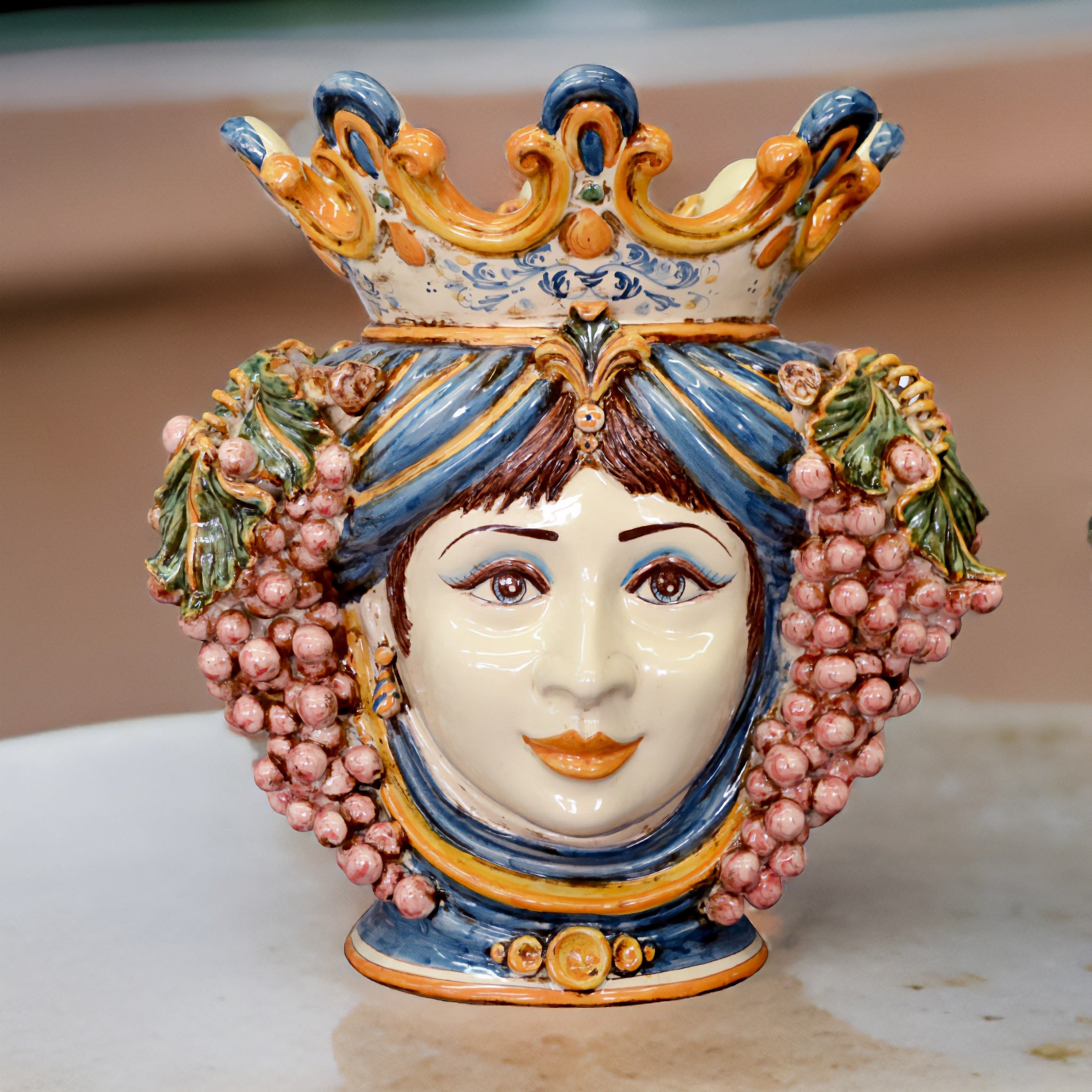 Testa di moro in ceramica di Caltagirone fatta a mano con decorazioni blu, gialle e grappoli d'uva rosa