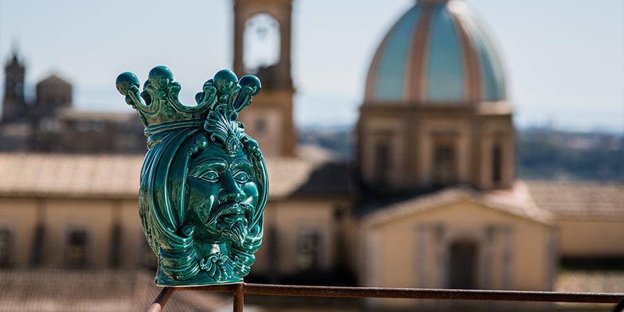 Ceramiche Caltagirone fatti a mano, testa di ceramica verde con corona davanti a edificio storico sfocato