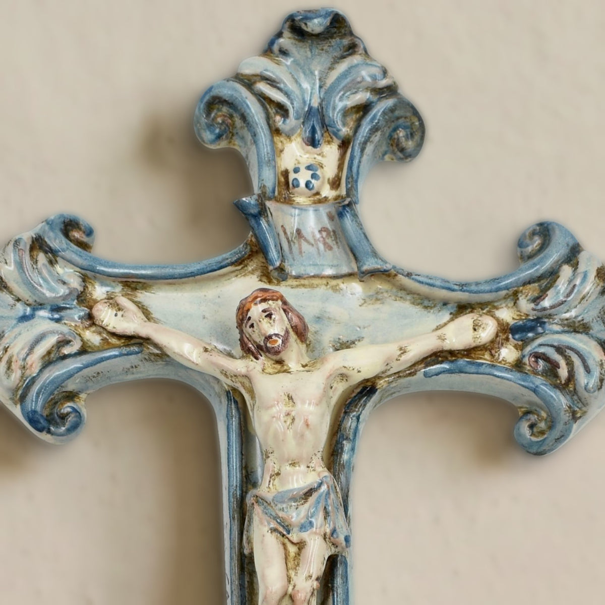 Close-up of the Mono Blue Caltagirone ceramic crucifix on the wall: Christ in relief, INRI scroll and top with blue scrolls