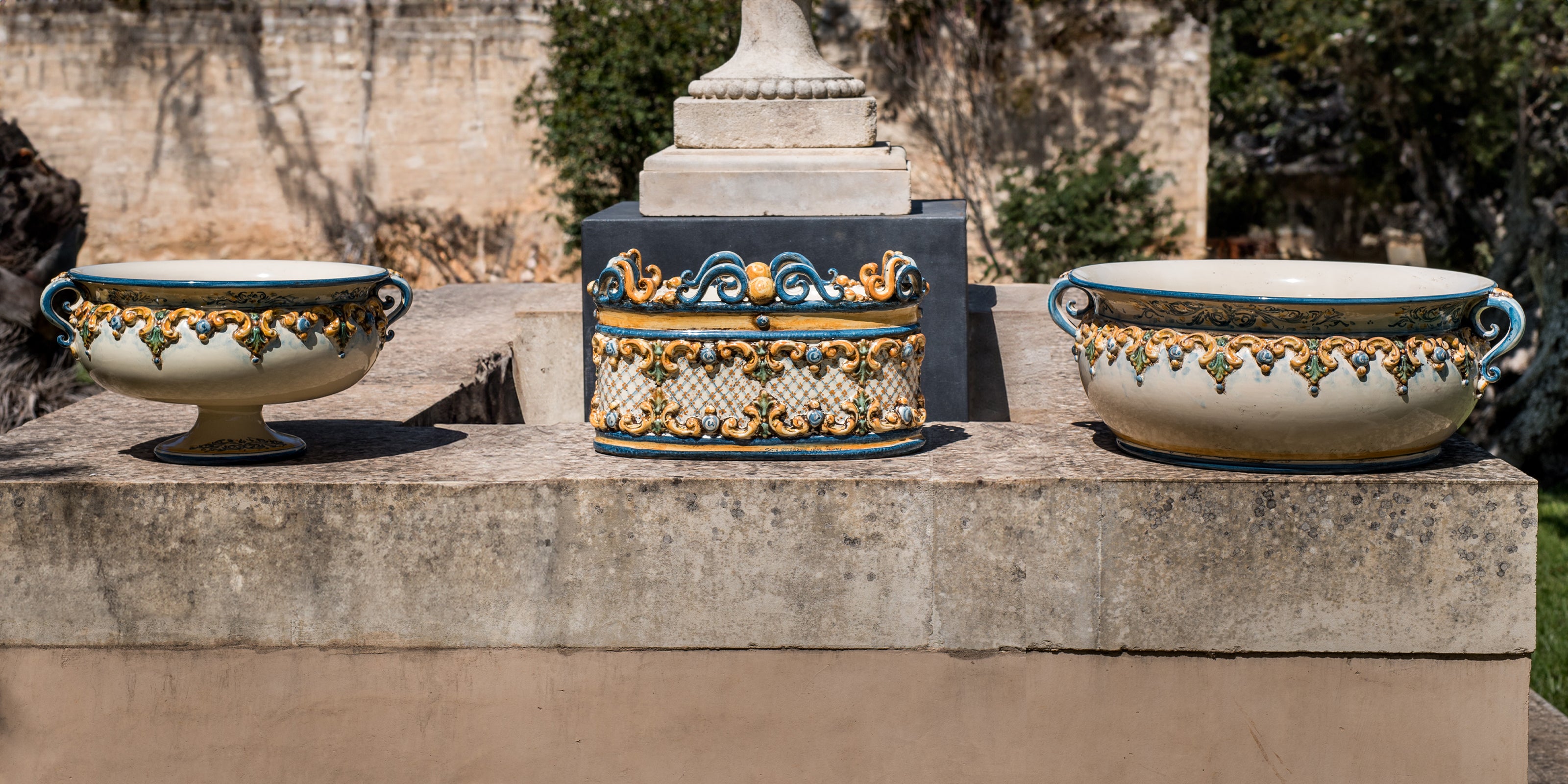 Alzate e Centrotavola in ceramica fatta a mano sono appoggiate su un muretto. Lo stile delle ceamiche di Caltagirone è classica in blu e arancio