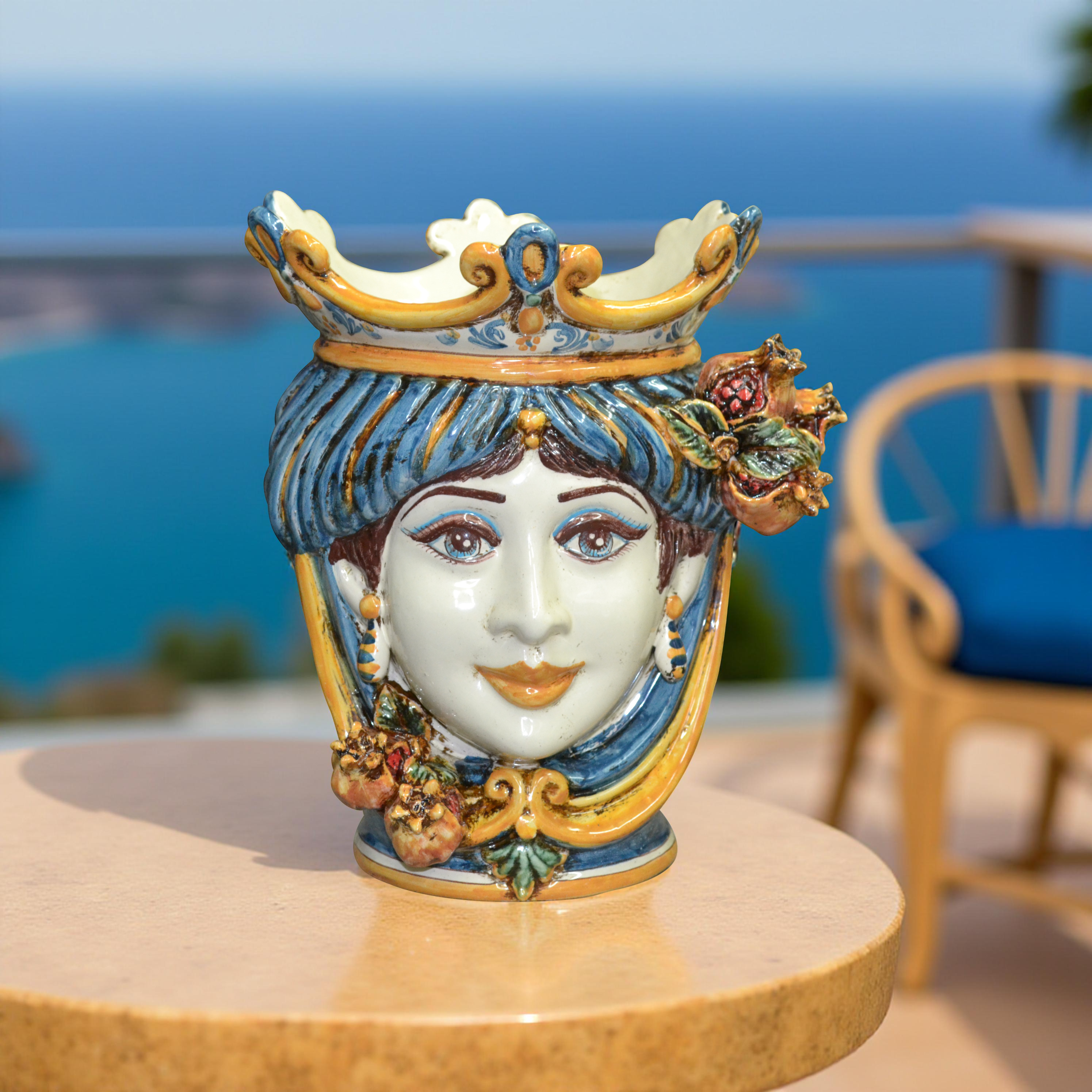 Vaso ceramica Caltagirone fatto a mano a forma di testa di donna con corona e decorazioni di melograni su tavolo all'aperto con vista mare